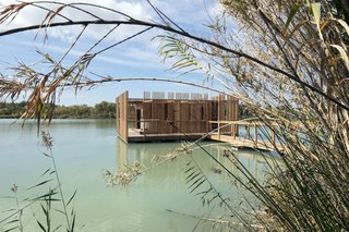 The architecture evokes a rustic construction in the midst of the lake's reeds.