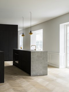 The minimalist kitchen in smoked oak with bronzed brass handles was designed by Norm Architects for the Danish kitchen manufacturer Reform, and is complemented by a sculptural kitchen island in a light gray ceramic stone, as well as a herringbone floor.