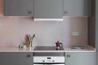 The kitchen cabinets are finished in a warm gray, and are fitted with vintage, brass concave handles. The countertops are a pink terrazzo-like quartz.