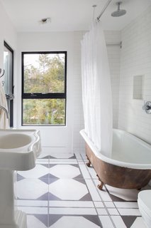 A Renovated Farmhouse in the Hamptons Hits the Market at $2.8M - Photo 9 of 13 - A clawfoot tub and graphic black and white tiles outfit one of the bathrooms.