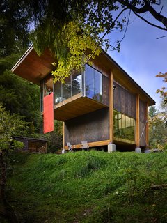 Reclaimed Materials Make Up This Artist Studio in Washington - Photo 6 of 6 - The home hovers above the ground on concrete bases, so as not to intrude too heavily on the natural landscape. The red hatch door from the loft bedroom is lowered in this image. 