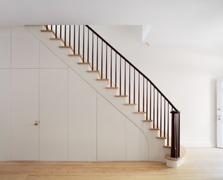 The main staircase at the center of the house creates a gracious ascent from the open living room and kitchen at the parlor level to a library and bedrooms on the upper levels. The stained walnut handrail adds a traditional look, but boasts a clean, modern treatment. Wood paneling envelops a discreet door that leads to the cellar. 