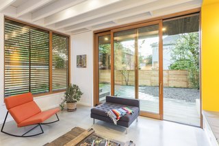 The material palette is simple and designed to age gracefully, featuring stained cedar siding and bright interiors with exposed ceiling structures and pops of primary colors throughout. 