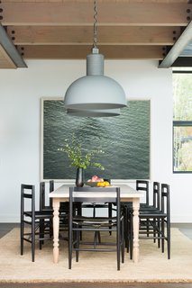 The dining room table is a new, custom-made piece from Nickey Kehoe. It is paired with ebonized black wood chairs with leather sling style seats by Sawkille Co. The chunky braided jute rug with fringe is from Armadillo & Co., the large pendant lights are from Frezoli Lozz, and the artwork is a photograph by Richard Misrach. <br>