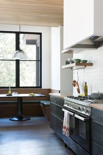 A six-person breakfast banquette was crafted from walnut wood. The table was custom-made by ABD Studio and has a cold roll steel top with a turned wood base that has been ebonized black. The pendant light is vintage. 