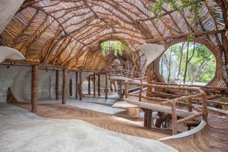 Sterkel's design for IK Lab continues the environmentally friendly spirit of the resort. Tree branches support the wavy canopy, while smaller sticks arranged in a diagonal pattern allow light to filter through. Large, round windows perforate the interior, and the floor is covered with a local, vine-like plant called Bejuco wood. 