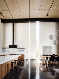 Within the setting of the open floor plan, slits of light reflecting on the ebonized, concrete floor help to demarcate distinct spaces. Here, the kitchen is set off from the dining and living areas. 