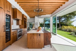 The customized walnut kitchen opens to the outdoors and features leathered Perla Venata Quartzite countertops and Miele appliances. 