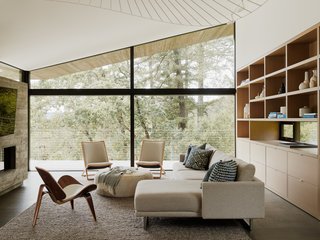 Large picture windows in the open living room frame the surrounding forest.