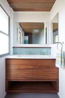 Walnut has also added warmth and contrast to the bathroom vanities. While the Heath Classic Field ceramic tile in Modern Blue has been used sparingly throughout the home, it still adds color to the hall bath vanity backsplash and at the shampoo niches in both bathrooms. 