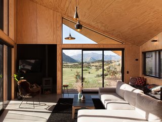 The contemporary interiors feature concrete floors and plywood paneling, with black accents that echo the cabin’s exterior. 