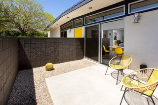 A mason block wall encloses a small front patio with access from the kitchen via a sliding glass door, creating a strong indoor-outdoor connection. 