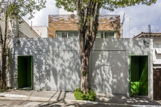 From the street, a discrete metallic wall features two green steel doors on either side. 