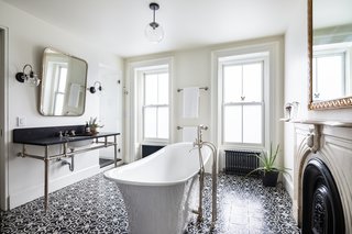 A beautifully designed, light-filled bathroom features a deep Victoria + Albert freestanding tub, an original marble mantle, a large black marble-topped vanity, and an encaustic concrete-tiled floor. 