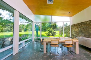 The dining area is surrounded by expansive glazing, with a stone wall that extends from the interiors straight outside the home.