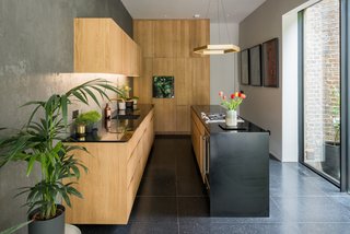 The kitchen pairs bespoke oak cabinetry with Gaggenau appliances and black Corian worktops that feature brass fittings by Vola for a polished, artistic look.