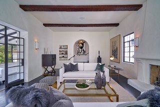 The elegant white-stucco living room is accented with exposed wood beams and anchored by a wood-burning fireplace. 