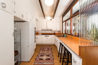 The original kitchen has vintage chrome hardware, a Western Holly oven, orange Formica counters, and cork flooring. 