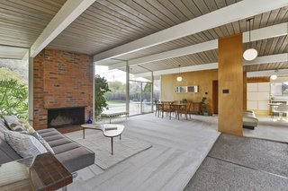 The well-preserved home features plenty of original details to please midcentury purists such as unpainted ceilings, wood paneling, aggregate floors, and an unpainted brick wood-burning fireplace. The signature open-plan great room is one of the high points of this light-filled property. 