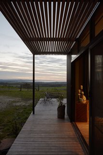 The prefab's external cladding is corrugated Colorbond in woodland gray; the pergola features natural timber hardwood battens. 