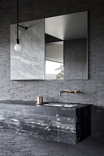 The bathroom wall tiles are a Japanese product from Inax, called Sekhia. The sink vanity is made from Black Marquina marble, and the aged bronze faucets were sourced from Brodware.