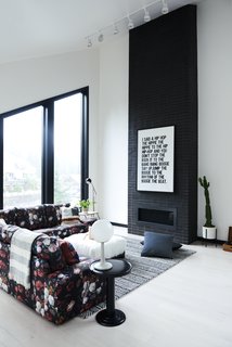 The open-plan living space is anchored by a black brick fireplace with a sleek modern profile. <span style="font-family: Theinhardt, -apple-system, BlinkMacSystemFont, "Segoe UI", Roboto, Oxygen-Sans, Ubuntu, Cantarell, "Helvetica Neue", sans-serif;">Muddox makes t</span><span style="font-family: Theinhardt, -apple-system, BlinkMacSystemFont, "Segoe UI", Roboto, Oxygen-Sans, Ubuntu, Cantarell, "Helvetica Neue", sans-serif;">he commercial wire-cut thin</span><span style="font-family: Theinhardt, -apple-system, BlinkMacSystemFont, "Segoe UI", Roboto, Oxygen-Sans, Ubuntu, Cantarell, "Helvetica Neue", sans-serif;"> bricks in ebony with liquid black added to the mortar mix. The Studio Floor Lamp is from Schoolhouse. </span>
