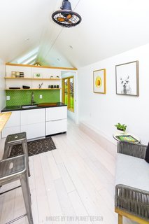 The minimalist open kitchen/dining/living room features a mostly neutral palette. A green tile backsplash provides a pop of color.