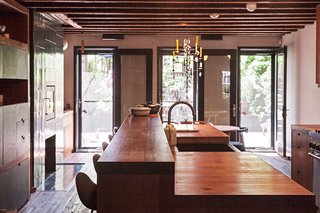 The fully updated garden-level kitchen features full-height glass doors that lead outside, reclaimed chestnut floors, teak countertops, and a Rais fireplace with Heath Ceramics tile.