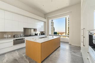 The custom gourmet kitchen has a center island, marble floors and countertops, white lacquer and oak cabinetry, stainless steel Miele appliances, and a view.