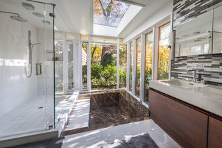 The updated master bath is flooded with natural light thanks to floor-to-ceiling windows and a skylight above. The surrounding trees provide users with privacy. 