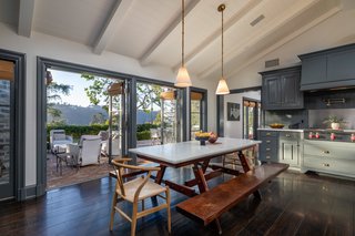 The elegant kitchen has vaulted tongue-and-groove ceilings paired with chic steel-gray cabinetry and white marble countertops. French doors open the room to a sunset-facing terrace with an outdoor fireplace and sweeping views across the canyon.