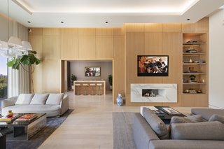 The high-ceilinged living space is designed for comfortable entertaining and features light wood paneling, a marble-framed fireplace, and an elegant bar off to the side.