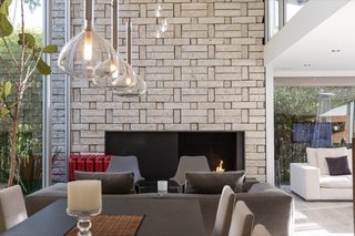 The double-height space is anchored by a brick fireplace with a midcentury vibe.&nbsp;