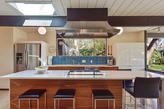 The updated kitchen has walnut-paneled cabinetry, quartz countertops, a turquoise tile backsplash, and a large center island with seating.