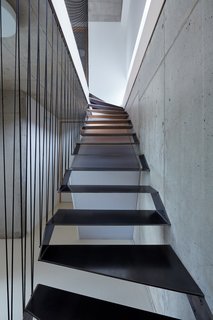 Dům Ve Svahu's staircase cuts through the house, the metallic tread contrasting with the concrete walls and netted railing. The architects, masparti, allowed the rest of the home to be light and airy in comparison by keeping furnishings spare and walls painted white.