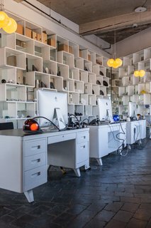 White metal desks are lit by a desk lamp variation from Bocci's 28-series. Behind them, open bookshelves act as room dividers.