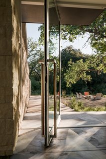  A metal-and-glass door with a modern-but-industrial edge ties into the home's material palette of pre-weathered corrugated steel cladding, buff limestone walls, and large aluminum apertures, along with an interior palette of cedar-clad ceilings, oil-rubbed steel, and exposed concrete floors.