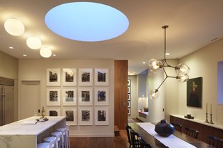 A dining room and kitchen benefit from the pale blue light that comes in through a skylight at dusk.