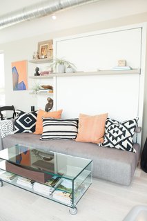 Monogram Modern Home Tour Takes On the West Coast - Photo 3 of 8 - The transforming wall bed system and accompanying glass coffee table by Resource Furniture modeled a space-saving solution for compact quarters. As the home travels from stop to stop, its furnishings evolve to conversate with the aesthetic of the host city. <span style="line-height: 1.8;">For San Francisco, Courtney Lake of Monogram Decor used a palette of blue, orange, and gold to evoke a youthful energy and recall the Golden Gate Bridge spanning bay waters.</span>