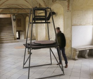 A motor runs a weighted grinder over the tabletop, creating a moving meditation of continuous time and process.