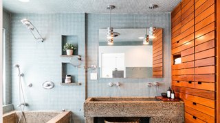 Luxurious amenities outfit the master bathroom, where wood shelving provides a warm counterpoint to blue tiles and a concrete sink and tub.