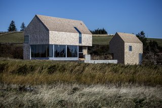 The northern side presents a traditional face of shingles and gabled roof while the southern side incorporates tall glass windows. The buildings are raised on concrete fin foundations that reduce their environmental impact.