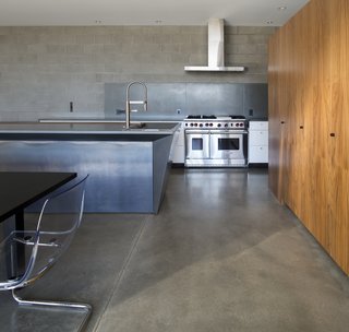 The downstairs communal living spaces flow freely between kitchen, dining room, and living room. Concrete block walls and polished concrete floors emphasize the heavy materiality that supports the visual lightness of the upper story.