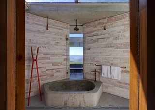 An Internationally Celebrated Home in the Australian Backcountry Asks $9M - Photo 7 of 13 - A centrally placed bathroom features an oversized concrete tub and bespoke brass and copper fixtures. A slim pane of glass allows you to take in views beyond the open terrace and firepit, while the glass ceiling exposes the room to the changing sky.