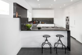 In a kitchen that Brunn built using Bosch appliances, an understated black-and-white palette is paired with a minimal design. The project was named Wrap It Up as an allusion to the way the Caesarstone runs up the wall to create a shelf. "Anytime we do a project," says Brunn, "we have to do something different and push the boundaries." The shelf also hides a secret compartment where the homeowner can slide in a cutting board for easy, accessible, and hygienic storage.