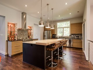 Custom Treefrog wood cabinets and quartz countertops outfit the kitchen, where a granite island with a built-in butcher block transitions into bar seating. Benson Pendants by Restoration Hardware hang above. Another frosted glass barn door leads to a walk-in pantry. 