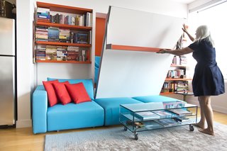 Van Duren demonstrates the ease of lowering the Swing, a queen-size wall bed with nine-foot sofa and sliding chaise. Here, it integrates with a shelving system, which continues the apartment's quirky motif of orange and blue. 