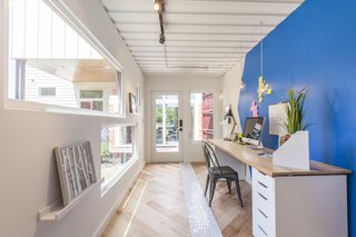 It's up to the homeowner to decide what to do with the additional 160 square feet; here, it's staged as an office. The shipping container features track lighting, wall sconces, a full-height cabinet to hang clothes, and a mini split air conditioner. The floors are a mix of engineered wood and hand-painted tile from Clay Imports. From inside the container, you can see through to the front of the house.