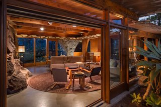 Find Seclusion in the City With This $2.5M Lloyd Wright Residence - Photo 2 of 7 - The integrated living and dining room is contained in an open, hexagonal space with 10-foot ceilings. A long stone wall contains a fireplace, which acts as a divider between the main room and the den. Powell removed the shag carpet that used to run throughout the house and replaced it with concrete topping.