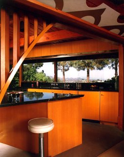 Find Seclusion in the City With This $2.5M Lloyd Wright Residence - Photo 4 of 7 - Powell removed a wall and walk-in pantry to allow the living and dining areas to flow into the kitchen, which is triangular with a granite countertop inlaid with aluminum terrazzo divider strips. He constructed an arched opening with the same radius in the stone arches in the adjacent exterior wall, keeping harmonious proportions throughout the home. The new, straight-grain fir cabinets match the ceilings as well.